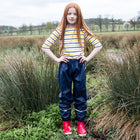 A girl stands in a grassy field wearing Puddleflex Waterproof Fleece Lined Trousers in navy with a striped top and red wellies.